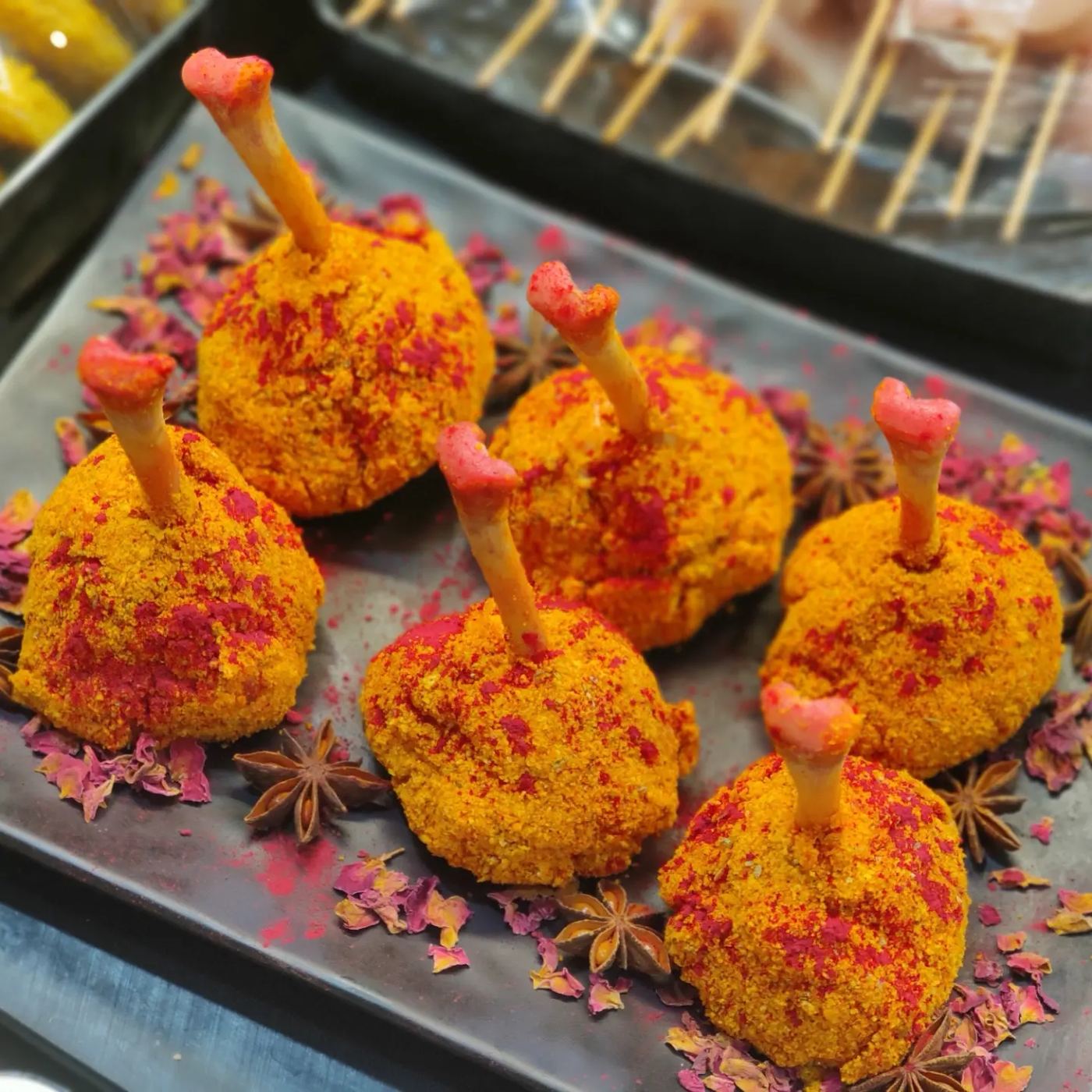 Spice-crusted chicken lollipops plated with dried rose petals and star anise