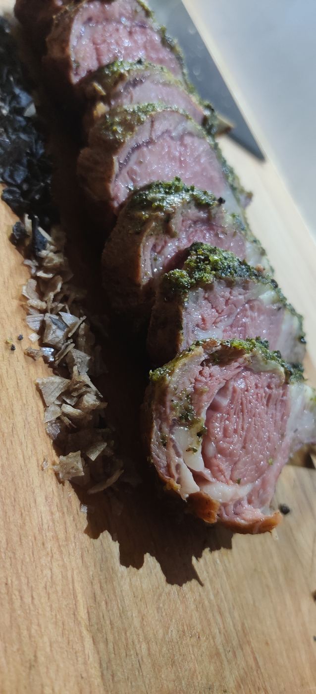 Herb-crusted meat sliced into rounds on a wooden board